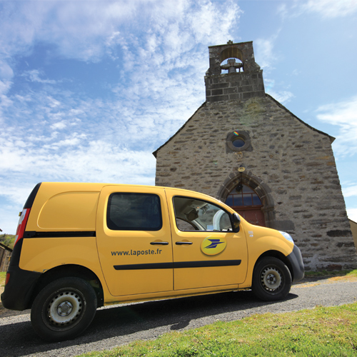 Yellow Kangoo car of a letter carrier of La Poste on top of a hill in front of a chapel