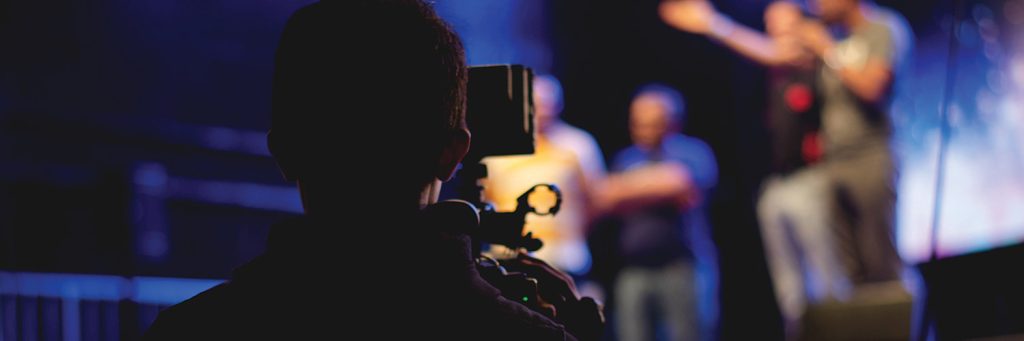 Person behind a camera filming people on a stage