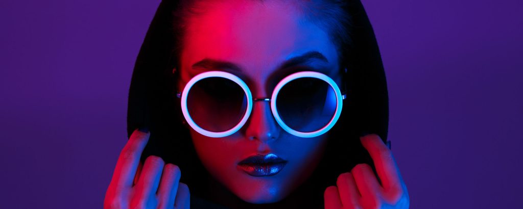 Front shot of a woman wearing neon sunglasses and a black hoodie