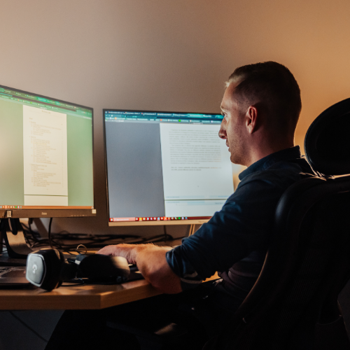 Person sitting at their desk, looking at two screens and typing on a keyboard