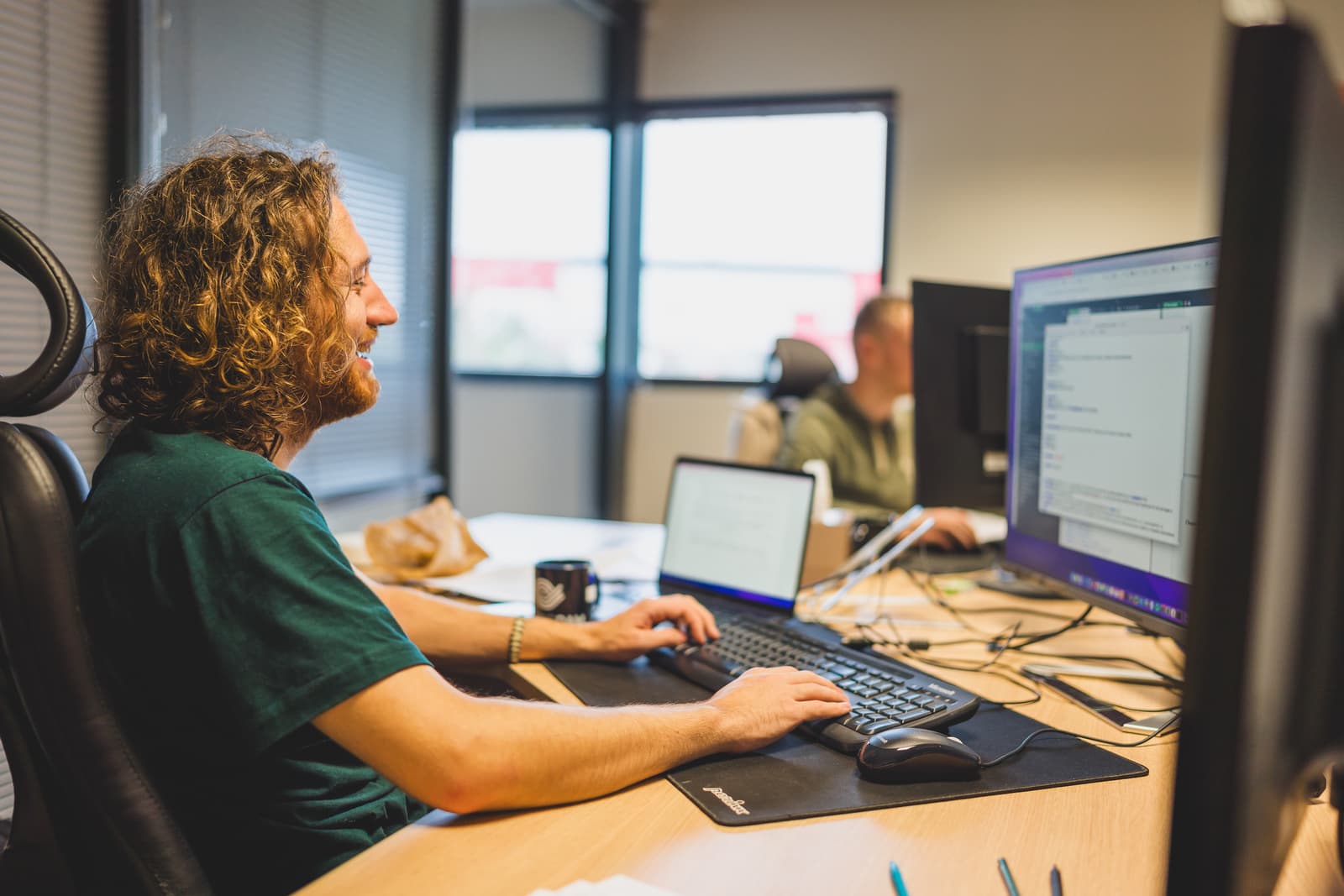 Two men sitting at their desks in front of their computers, smiling, working on the Ephoto Dam digital asset management solution.