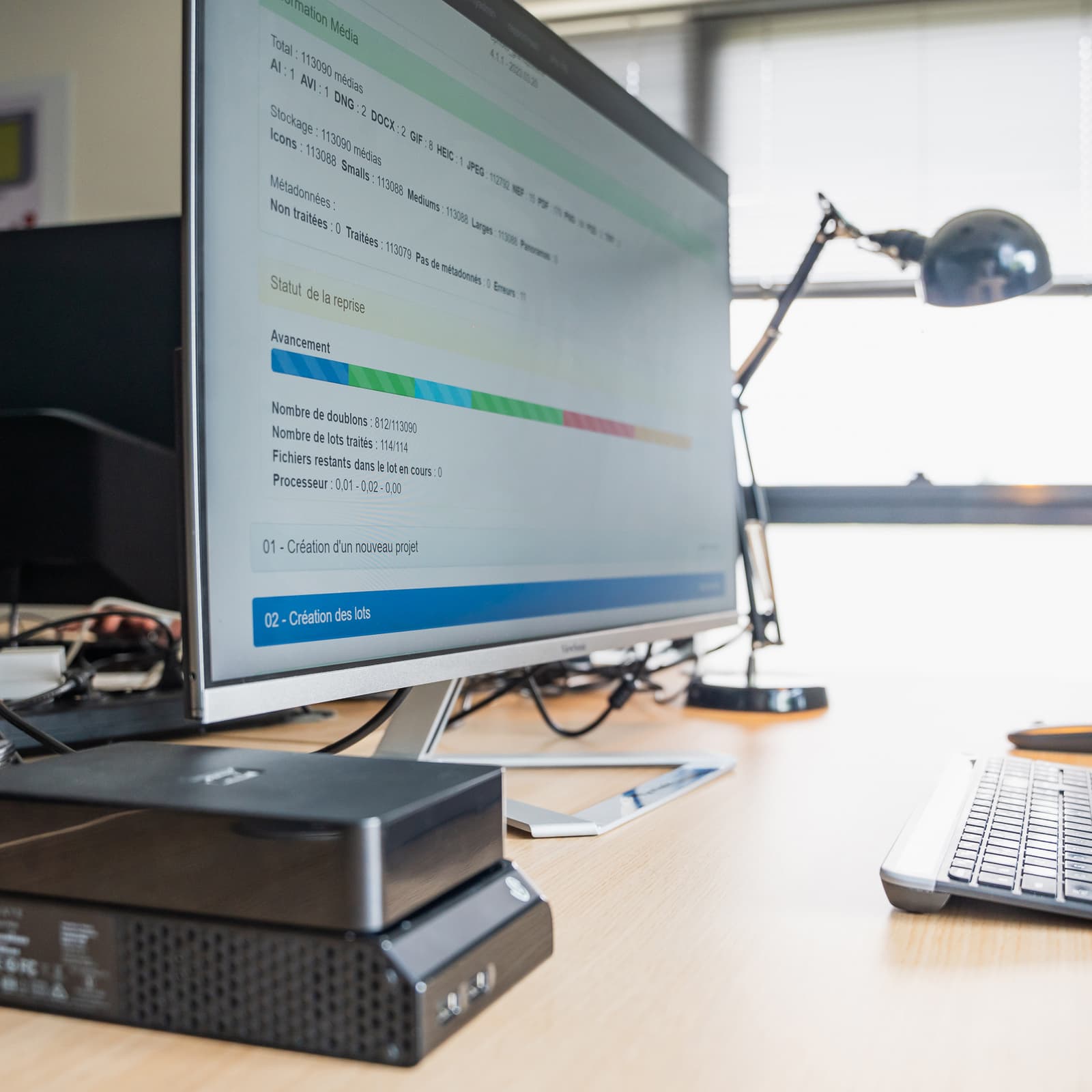 Computer on a desk with a keyboard, mouse, lamp and hard drives.