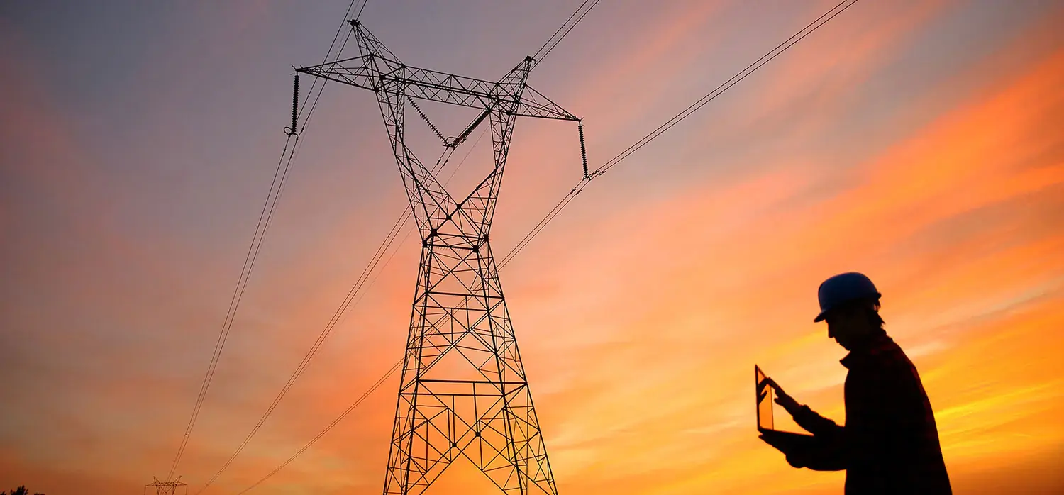 Electric pylon in a field where a man wearing a construction helmet is checking elements on his computer.
