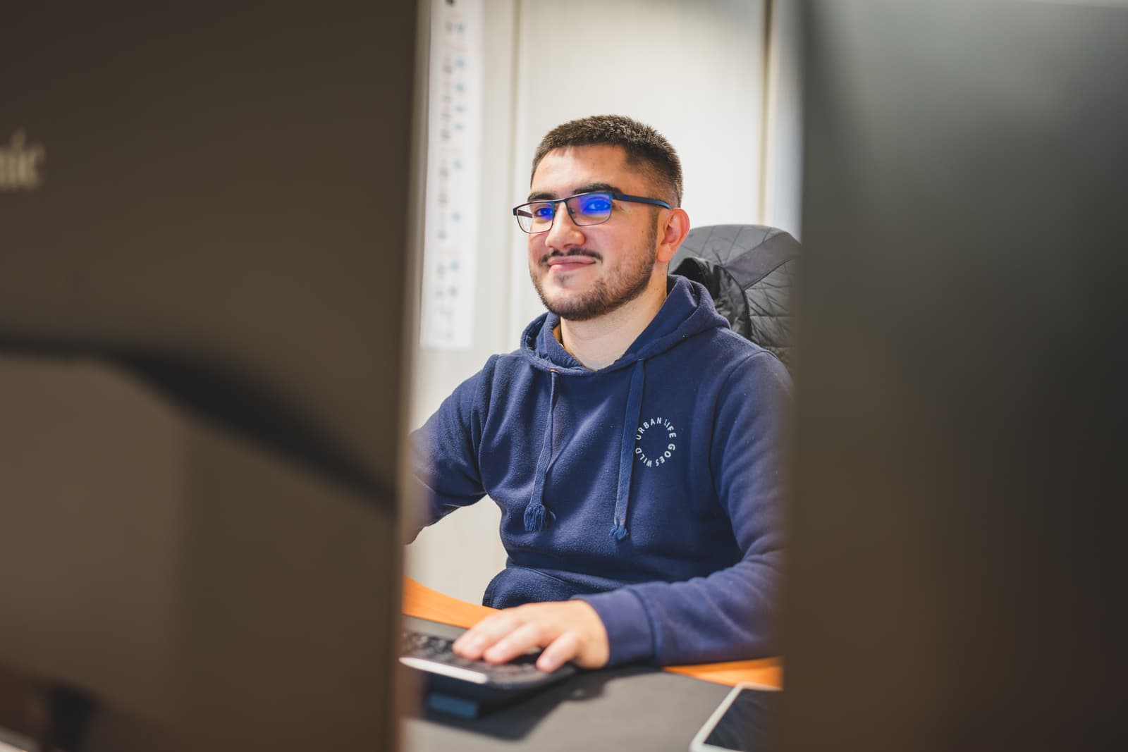 A smiling man wearing glasses sits in front of a computer, working on the Ephoto Dam software, a Digital Asset Management solution.