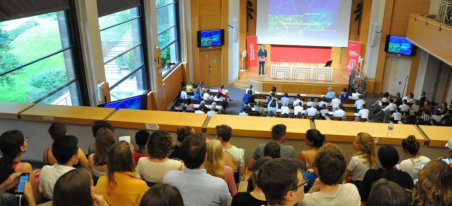 Amphitheatre on the premises of Sciences Po where hundreds of students listen to their professor speak from his podium.