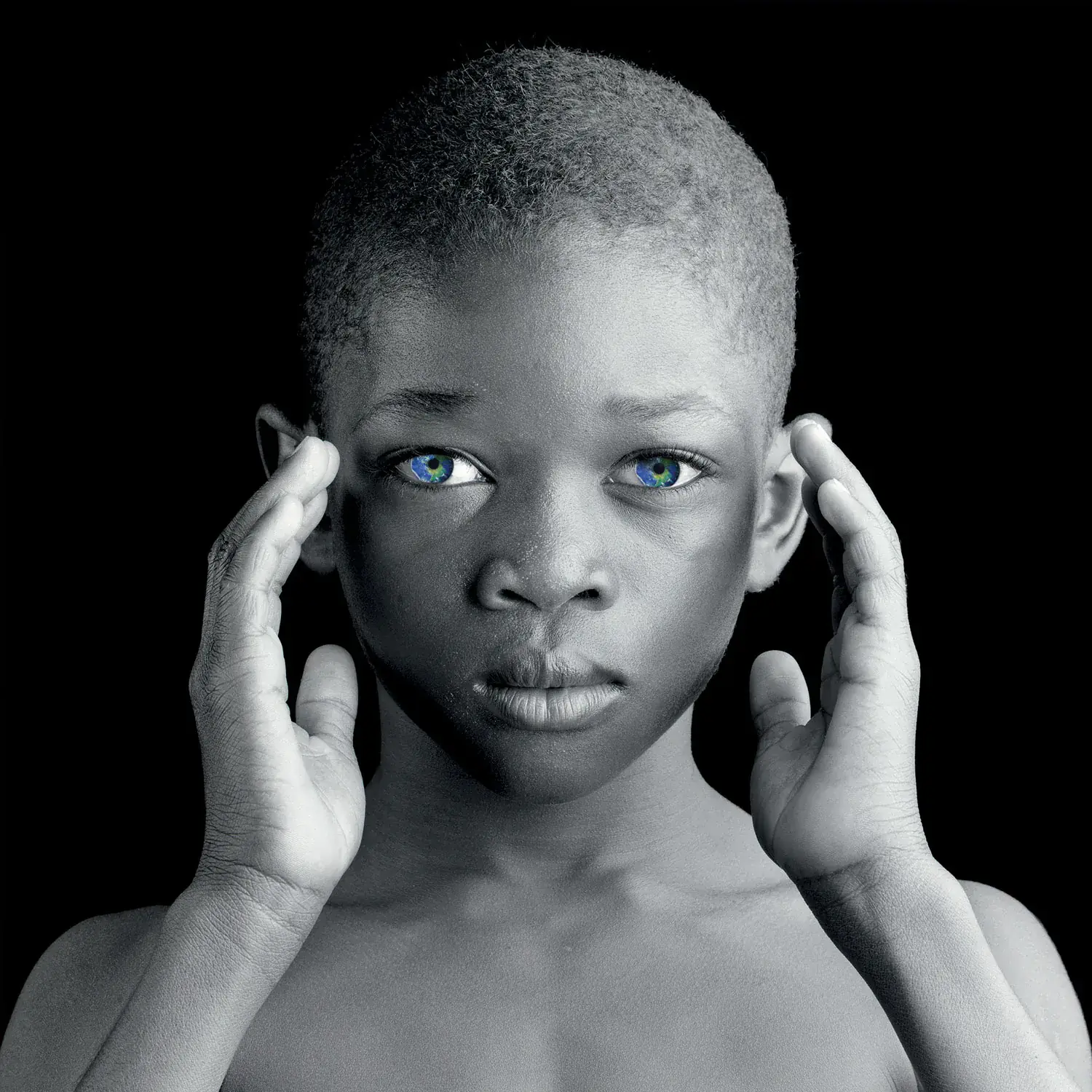 Black and white portrait of a child holding both hands to the edge of his face.